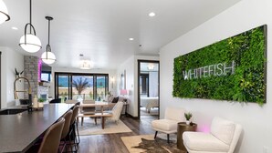 Una cocina moderna con barra, una sala de estar con un sofá blanco y una alfombra, y una pared con un jardín vertical de plantas y la palabra "WHITEFISH".