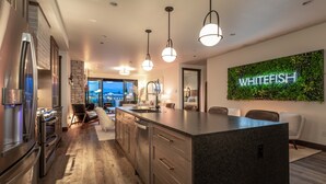 Una cocina moderna con electrodomésticos de acero inoxidable, una isla de granito e iluminación colgante.