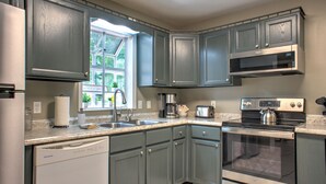 Una cocina con gabinetes grises, lavavajillas, estufa, microondas y ventana con vista a follaje.