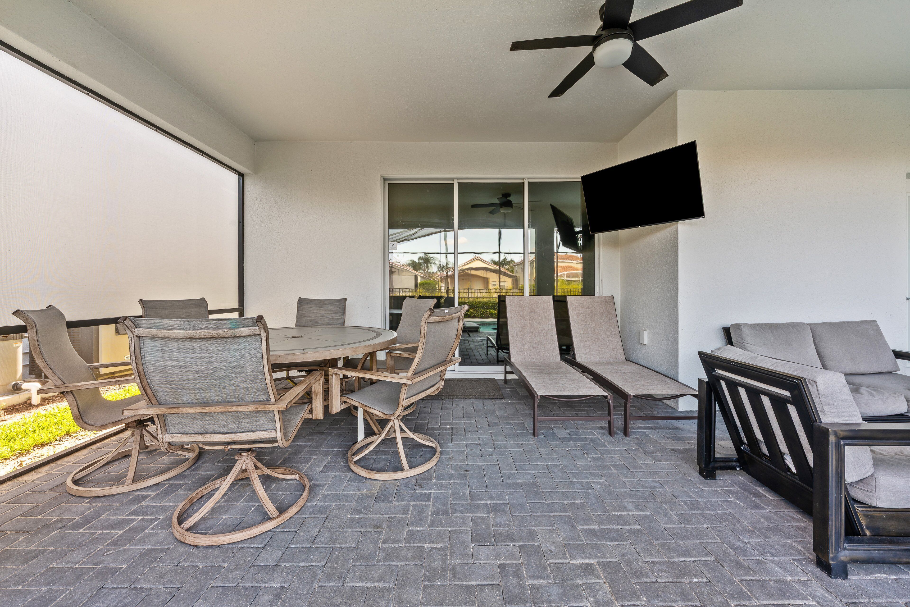 Een terras buiten met een eettafel en stoelen, een bank en een plafondventilator.