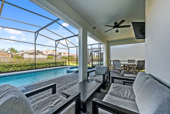 A covered outdoor area with a pool, seating, and a ceiling fan.