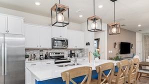 A modern kitchen with white cabinets, stainless steel appliances, a central island with bar stools, and pendant lighting.