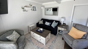 Sala de estar com sofá preto, poltrona estampada, mesa de centro e televisão fixada na parede.