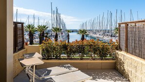 A balcony with a view of a marina filled with sailboats, a small table, and a chair.