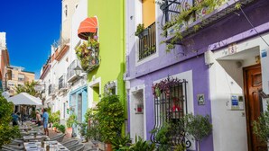 A narrow street with colorful buildings, outdoor seating, and potted plants. - CostaBlancaDreams - Alexia in Calpe (Calpe)