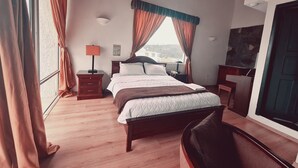 A hotel room with a large bed, wooden floor, a desk, a chair, a nightstand with a lamp, and a view through the window. - Hotel & Suites Gonsalez Suarez Quito (Quito)