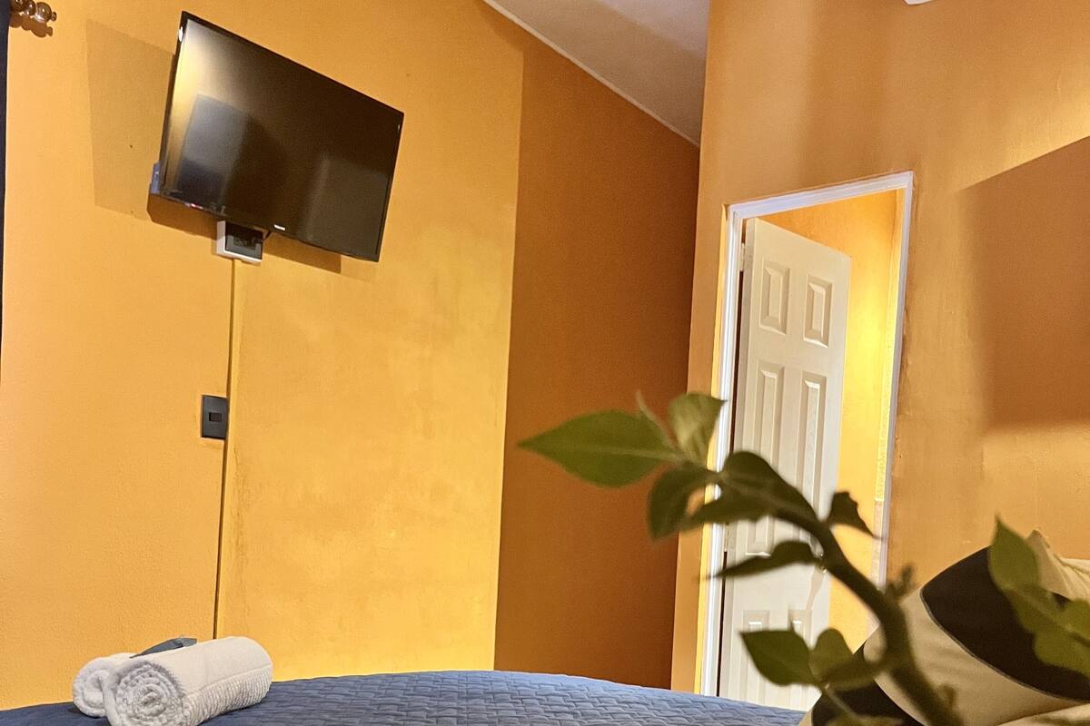Ein Hotelzimmer mit einem Bett, einem an der Wand befestigten Fernseher und einer Tür zu einem anderen Raum.