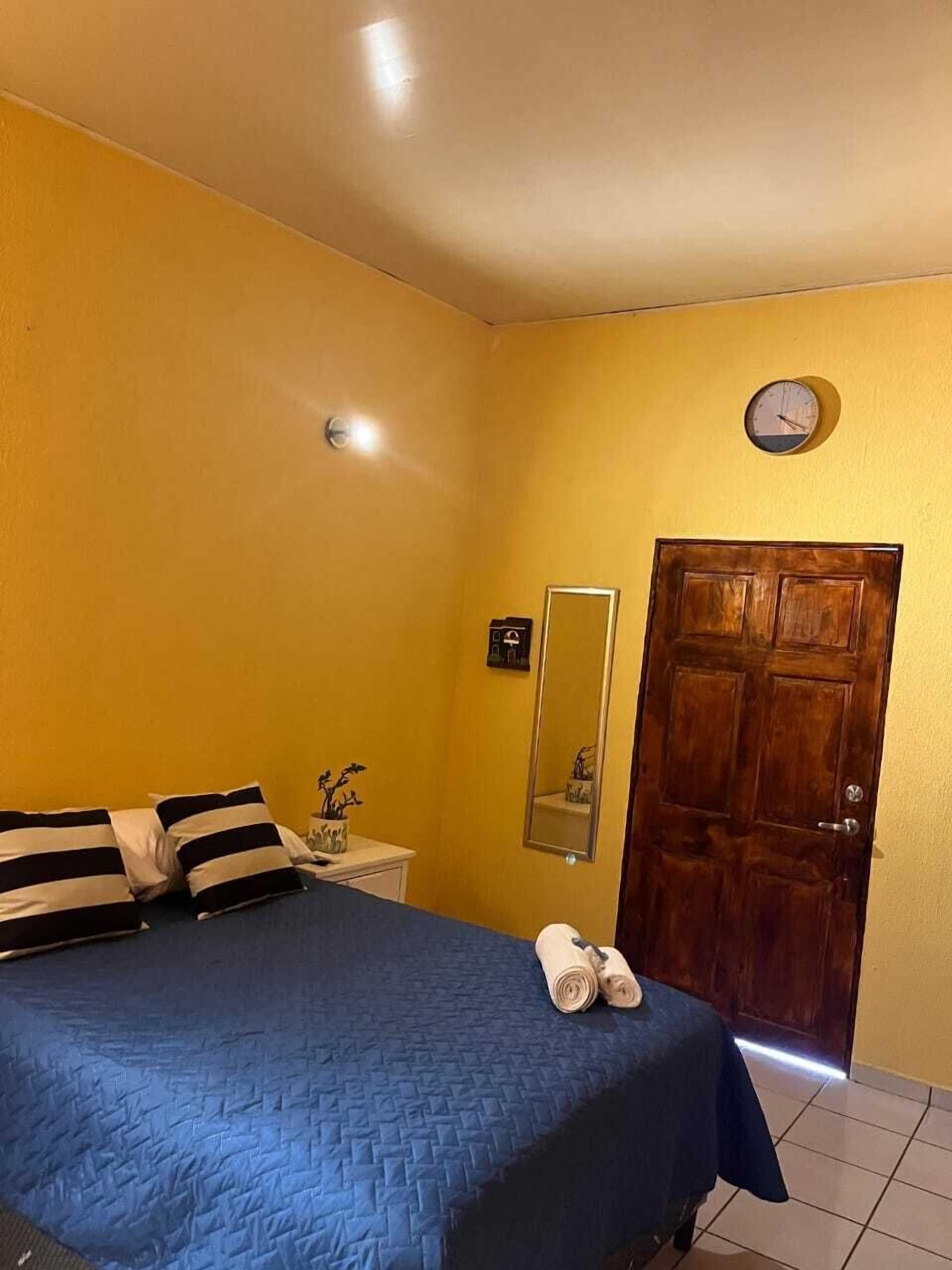 Une chambre à coucher avec un lit, une table de chevet, un miroir, une porte en bois et une horloge murale.