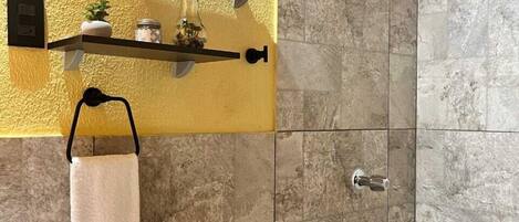 A bathroom with a shower, a toilet, a sink, and shelves with decorative items.