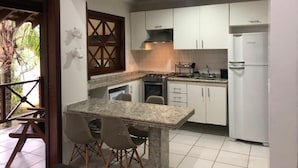 Una cocina compacta con armarios blancos, horno integrado y refrigerador. Cuenta con un pequeño comedor con mesa y sillas.