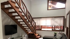 Una sala de estar moderna con una escalera de madera, un televisor de pantalla plana, un sofá y una ventana con vistas.