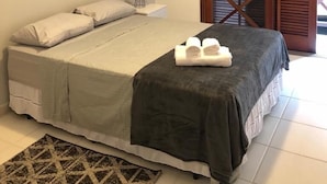 Un dormitorio con cama, mesita de noche, lámpara, dos obras de arte enmarcadas, equipo de aire acondicionado y puerta de madera con ventanal.