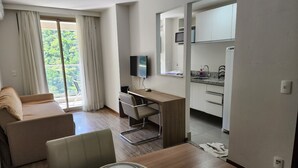 A modern apartment with a dining area, a sofa, a kitchen with a TV, and a balcony with curtains. - Flat near the river Center/Barra Olímpica (Rio de Janeiro)