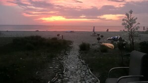 En strandscen med en stenig stig som leder ner till stranden, strandstolar och ett tält.