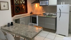 A compact kitchen with a granite countertop, white cabinets, a microwave, a stove, and a refrigerator.