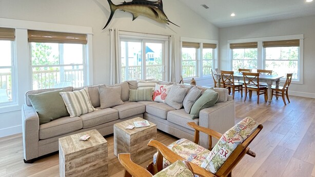 A spacious living room with a large sectional sofa, a wooden coffee table, and a dining area with a table and chairs. - The Beach Lily - South Cape San Blas - Pet Friendly (Port St. Joe)