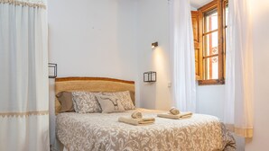Una cama bien hecha con un edredón estampado, dos lámparas de noche y una ventana con cortinas.