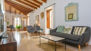 Amplia sala de estar con techo de madera, un sofá gris con cojines estampados, una mesa de centro y un espejo en la pared.