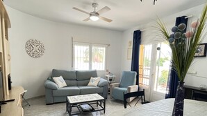 Una sala de estar con un sofá gris, una mesa de centro, un sillón azul y una mesa de comedor con mantel blanco.