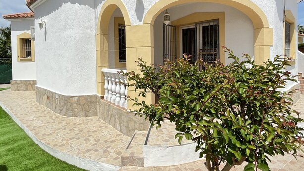 Un edificio blanco con arcos amarillos, una entrada con azulejos y un pequeño jardín.