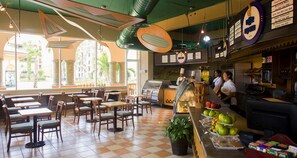 Un restaurant avec un sol à carreaux, des tables et des chaises en bois. On y trouve un comptoir avec un menu, et un grill est visible au fond de la salle.