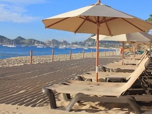 A beach with sun loungers and umbrellas, a sandy beach, and sailboats in the background. - New Listing - Medano Beachfront Luxury Villa - Walkable to Downtown Cabo! (Cabo San Lucas)