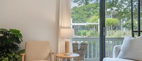 Una habitación con sofá, una silla, una mesita redonda, una lámpara y un ventanal con vistas a zonas verdes y edificios.