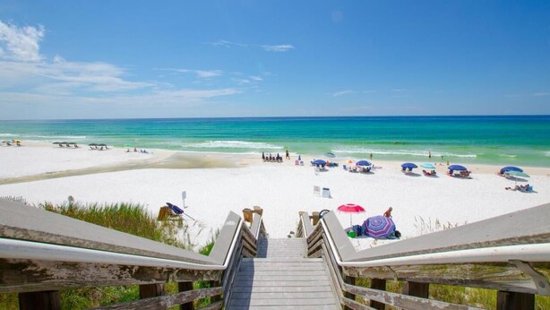 Een strand met een houten trap naar het zand, parasols en mensen.