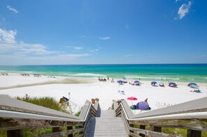 A beach with a wooden staircase leading down to the sand, umbrellas, and people.