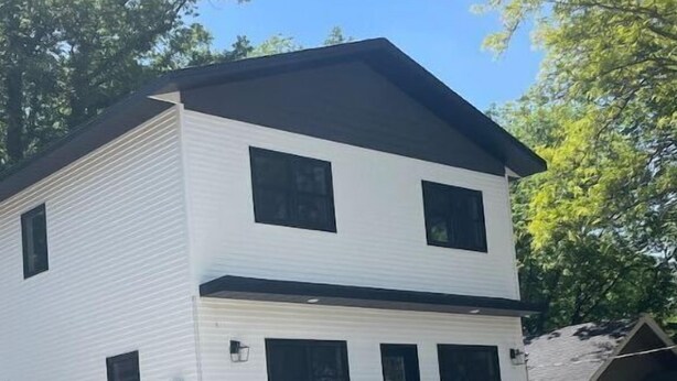 A two-story white house with a black roof, a front porch with chairs, and a visible garage. - Entire Top Floor Only: Okoboji Oasis/ Private Entrance (Arnolds Park)