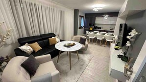 A modern living room with a black sofa, a round coffee table, and a dining area with white chairs.