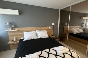 Un dormitorio moderno con cabecera de madera, colcha de diseño blanco y negro, y un espejo grande que refleja la habitación.