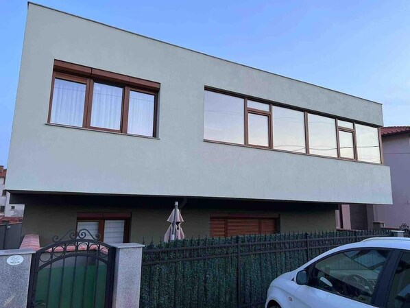 Un edificio de dos plantas con techo plano, ventanas grandes y entrada protegida por una reja.