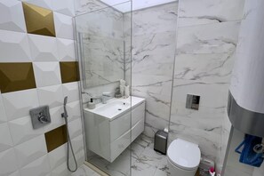 Un baño moderno con ducha envuelta en cristal, lavamanos blanco y retrete.