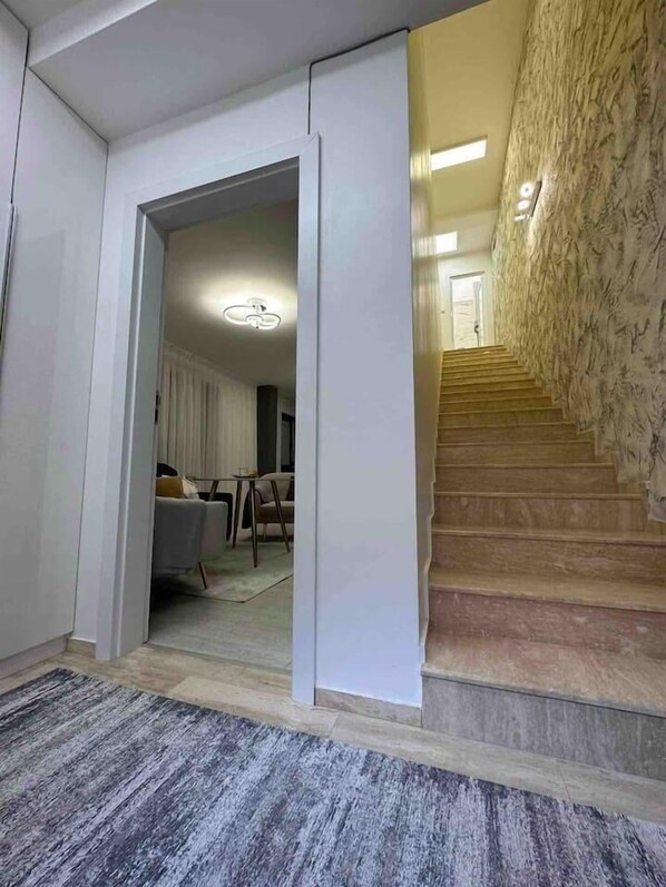 A hallway with a carpeted floor, a staircase with wooden steps, and a door leading to a room with a bed and a table.