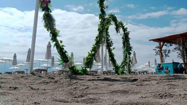A beach setting with a heart-shaped floral arch made of greenery and flowers.