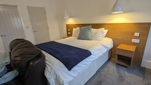 Hotellihuone, jossa on sänky, yöpöytä, tuoli ja vaatekaappi.