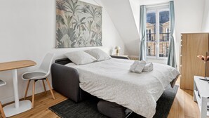A modern bedroom with a bed, a desk, and a large window with a view of buildings. - Lovely studio for 2 people in Paris (Paris)