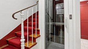 A staircase with red carpeted steps and white balusters, leading to a glass door with a sign. - Lovely studio for 2 people in Paris (Paris)