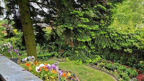 Un jardin avec différentes plantes et fleurs, un arbre et une zone dallée.