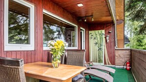 Un espace extérieur abrité, avec une table en bois, des chaises en osier et un extincteur.