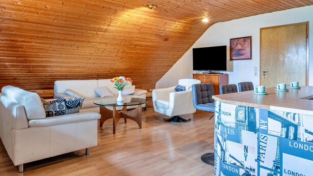Un salon moderne avec un plafond en bois, des canapés blancs, une table basse en verre et un coin bar décoré avec un motif représentant un paysage urbain.