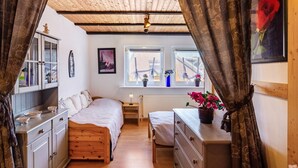 Une chambre avec un plafond en bois, un lit, une commode, une fenêtre avec des stores et un radiateur.