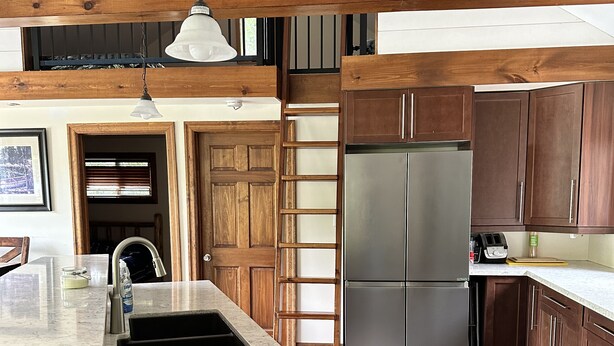 Una cocina con encimera de mármol, armarios de madera, un refrigerador de acero inoxidable y una lámpara colgante.