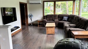 Amplia sala de estar con un sofá modular grande, un televisor de pantalla plana montado en la pared, una mesa de centro de madera y un ventanal con vistas al exterior.