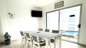 A dining area with a table and chairs, a ceiling fan, a TV mounted on the wall, and a view of a swimming pool through a glass door.