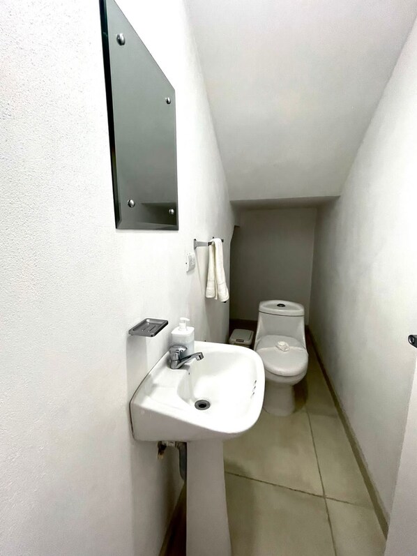 Un baño estrecho con un lavamanos blanco, un espejo y un inodoro.