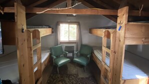 A cabin with bunk beds, a small table, two chairs, a window, and a patterned rug.