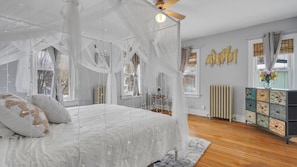 Quarto com cama de dossel, radiador, um armário decorativo e vista para o exterior.