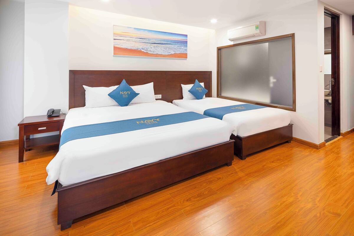 Een hotelkamer met twee bedden, een houten vloer, een schilderij aan de muur en een grote spiegel.